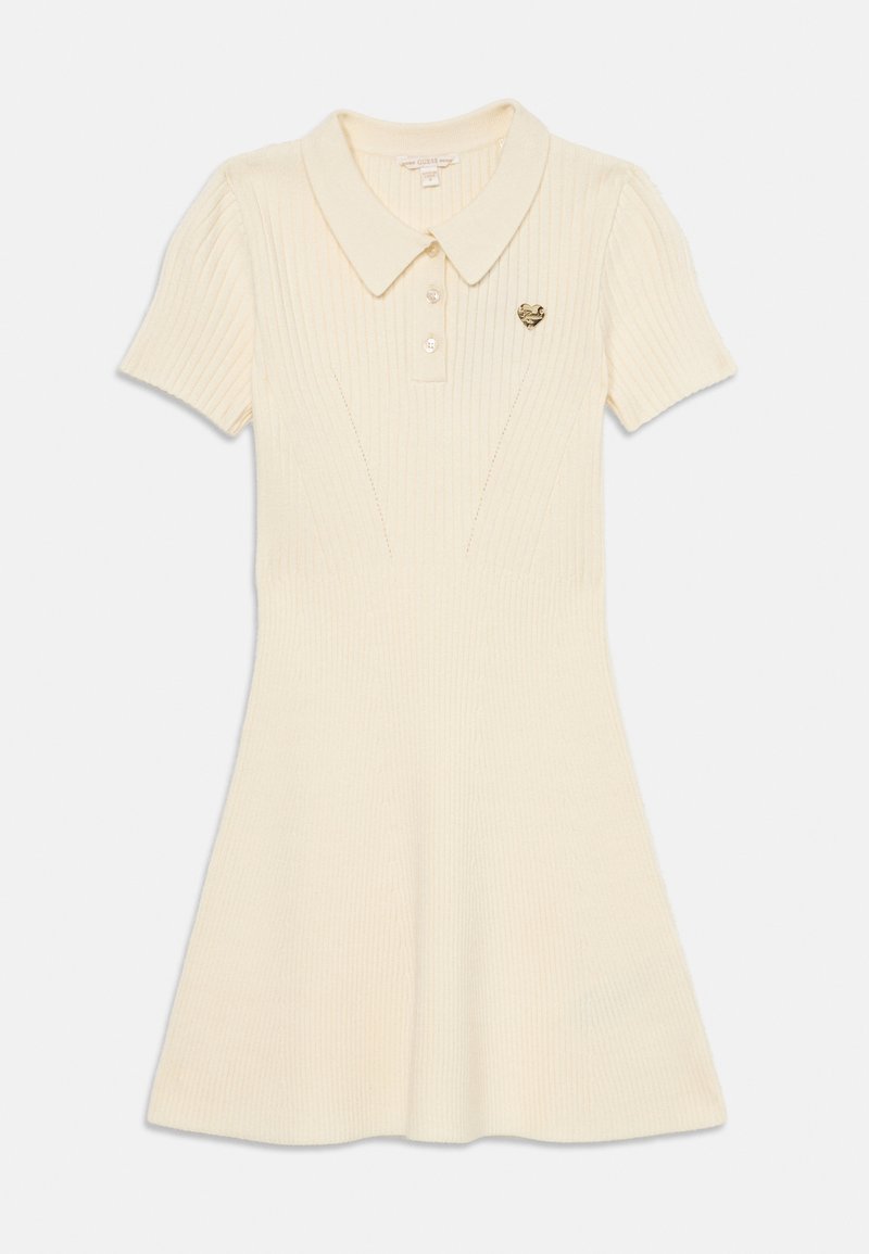 Korte ermed polo kjole i kremfarge, ribbet tekstur, fitted overdelen, utflared skjørt, har krage og et lite gyllent emblem på brystet.