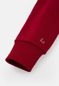 Czerwona bawełniana bluza z długim rękawem z prążkowanym mankietem oraz małym złotym logo w okolicy nadgarstka. Gładka faktura i dopasowany krój.