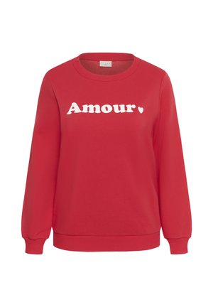 Punane pikkade varrukatega dressipluus ümara kaelusega. Kaunistatud sõnaga "Amour" paksudes valgetes tähtedes ning väikese südamekujundusega.