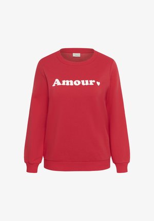 Punane pikkade varrukatega dressipluus ümara kaelusega. Kaunistatud sõnaga "Amour" paksudes valgetes tähtedes ning väikese südamekujundusega.