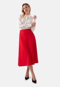 Witte blouse met lange mouwen en kraag, gecombineerd met een rode A-lijn midi rok. Zwarte hoge hak schoenen complementeren de outfit. Soepele stoftextuur.