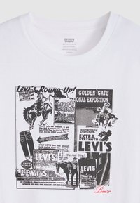 Λευκό βαμβακερό μπλουζάκι με μαύρο γραφικό εκτύπωμα που περιλαμβάνει vintage διαφημίσεις της Levi's, εικόνες καουμπόηδων και κόκκινο κείμενο Levi's.