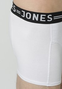 Weiße Baumwollboxershorts mit einem schwarzen elastischen Bund, auf dem in weißer Schrift "JONES" steht, darunter zwei dünne weiße Streifen.