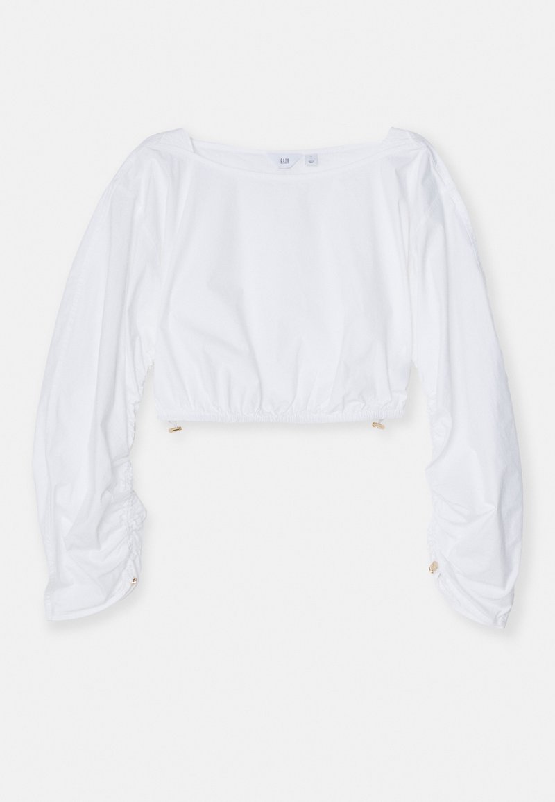Top branco cropped com mangas longas em balão, apresentando punhos elásticos e uma cintura franzida. Feito de um tecido leve e suave.