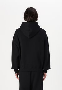 Felpa nera con cappuccio, dal taglio relaxed fit, spalle scese e polsini a coste. Tessuto morbido con un design minimalista, senza loghi visibili.