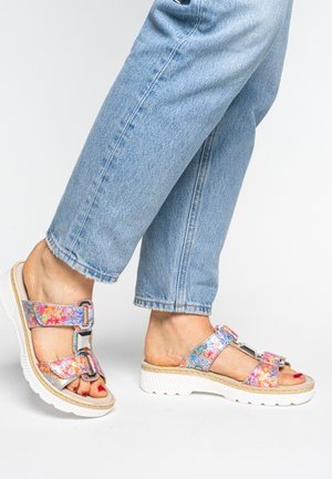 Feet wearing colorful floral sandals with thick white soles, paired with cropped light blue denim jeans against a plain background.
