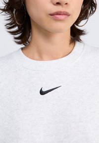 Sweatshirt gris clair en tissu doux, arborant un logo Nike en noir sur la poitrine et un design classique à col rond.
