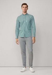 Groen en wit gestreept overhemd met een staande kraag, gecombineerd met grijze sweats. Schoenen zijn wit met een blauwe acccent.