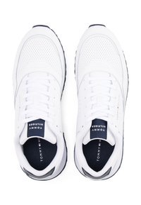 Baskets de sport blanches avec tige perforée, lacets plats, accents bleu marine et semelle rembourrée, arborant un logo sur la languette et la semelle intérieure.
