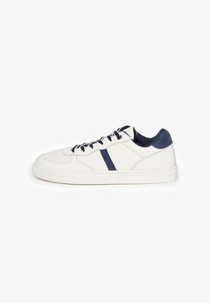 Sneaker blanche basse avec lacets bleu marine, talon et bande latérale, présentée sur un fond blanc.