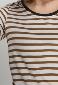 Camiseta de rayas en blanco y marrón, con mangas cortas y un cuello negro brillante. Textura suave con rayas horizontales de diferentes anchos.