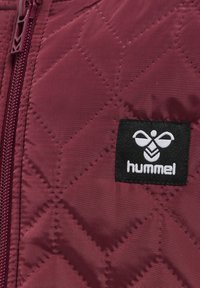 Bordeauxfärgad vadderad jacka med diamantmönster, med en framsida med dragkedja och en svart Hummel-logotyp på vänster sida. Slät textur.