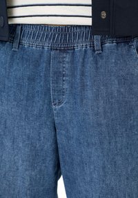 Blauwe denim broek met elastische taille, gedragen met een gestreept shirt en een donker jack met drukknoopsluiting.