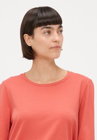 Koraalkleurig overhemd met lange mouwen en een ronde halslijn, met een zachte textuur. Eenvoudig ontwerp in een effen kleur, geschikt voor veelzijdige styling.