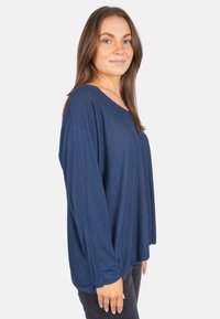 Marineblaues Langarmshirt mit entspannter Passform und weitem V-Ausschnitt, aus einem weichen, leichten Stoff gefertigt. Nähte an den Ärmeln sichtbar.