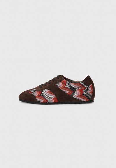 Brown suede sneaker featuring a zigzag pattern in red, black, and white woven fabric, with black laces and a rubber sole.