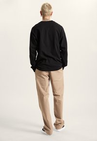 Maglietta nera a maniche lunghe e pantaloni beige. La maglietta ha una vestibilità comoda, mentre i pantaloni sono a gamba dritta con una superficie liscia e tasche laterali.