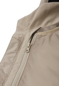 Gros plan sur la fermeture éclair d'une veste beige avec des détails de tissu et de couture sur les couches extérieure et intérieure.
