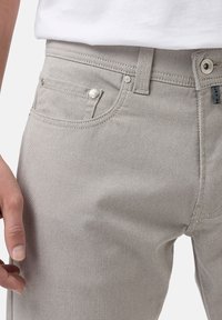 Hellgraue Denim-Jeans mit strukturierter Oberfläche, Fünf-Taschen-Design, Metallzubehör und einem sichtbaren Markenschild am Bund.