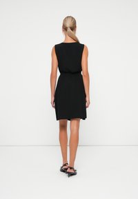 Robe noire sans manches avec une taille cintrée, un ourlet au genou et une texture lisse. Elle présente une ceinture à nouer subtile et un design simple et épuré.