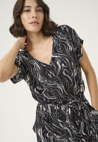 Black and white patterned short-sleeve top with a V-neckline and a tie waist. The fabric has a smooth texture with abstract wave designs.