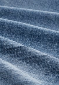 Țesătură denim într-o nuanță de albastru mediu, având o suprafață moale, texturată, cu modele țesute vizibile și variații subtile de culoare.