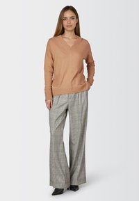 Light brown, V-neck sweater with front pockets paired with gray plaid wide-leg trousers, featuring a high waist and smooth texture.