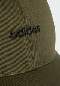 Olive green baseball cap made of textured fabric featuring black embroidered "adidas" logo on the front. Curved brim, stitched detailing visible.