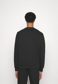 Felpa nera con collo rotondo, maniche lunghe e polsini a costine. Texture liscia, design minimalista, senza loghi o motivi visibili.