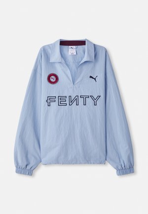 Vaaleansininen pitkähihainen paita, jossa on käännetty kaulus, "FENTY"-logo ja pyöreä punainen merkki logolla, suunniteltu Puman toimesta.