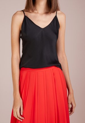 Sorte satin camisole med tynde stropper, med en V-udskæring, parret med en rød plissert nederdel, der fremhæver glatte teksturer og en livlig farvekontrast.