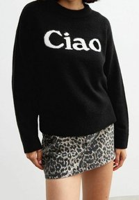 Schwarzer Strickpullover mit "Ciao" in weißem Text, kombiniert mit einem figurbetonten Minirock im Leopardenmuster. Weiche Textur, runder Ausschnitt und lange Ärmel.