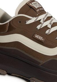Baskets Vans marron avec bande latérale blanche, lacets blancs et marron, semelle noire épaisse, affichant le logo Vans sur la languette et le côté.