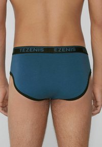 Blaue Baumwollslips mit schwarsem Bund, der das 'TEZENIS'-Logo trägt. Das Design umfasst glatte Kanten und einen engen Sitz. Minimalistischer Stil.