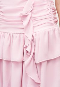 Vestido rosa claro con tela fruncida y detalles de volantes en capas a lo largo de la cintura y la falda.