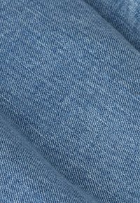 Gros plan sur un tissu en denim bleu clair texturé avec un motif de tissage diagonal visible et de doux plis.