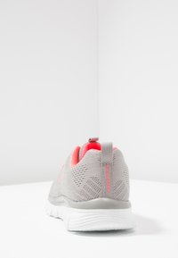 Graue Sportschuhe mit pinken Akzenten, ausgestattet mit einem Mesh-Obermaterial, gepolstertem Kragen und strukturiertem Fersenbereich. Leichte Sohle mit ausgeprägtem Profil.