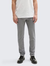 Calças cinzas ajustadas em um tecido texturizado com um padrão sutil, combinadas com sapatos pretos de atacadores. Usadas com uma t-shirt branca simples.