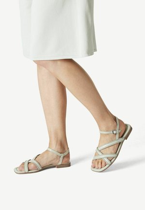 Light grey leather sandals feature crisscross straps and a buckled ankle strap, with a flat sole and open toe design.