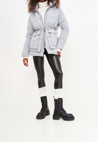 Lichtgrijze donsjas met een getailleerde taille, ritssluiting en twee voorzakken. Gecombineerd met zwarte legging en zwarte veterboots in combatstijl.