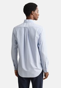 Világoskék, gombos ing klasszikus gallérral, hosszú ujjakkal, íves aljú és finom textúrával. A háton egy hajtás található.