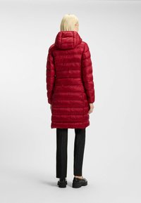 Röd puffjacka med horisontell quiltning, parat med svarta randiga byxor och kraftiga svarta skor; har en huva och en medellång snitt.