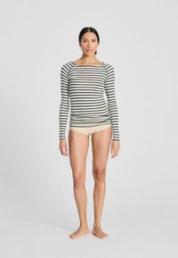 Langærmet stribet top med sorte og cremefarvede vandrette stribemønstre, let materiale, rektangulær halsudskæring og tætsiddende design. Båret med nude undertøj.