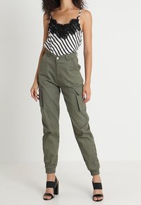 Raidallinen mustavalkoinen toppi pitsireunuksilla, yhdistettynä oliivinvihreisiin cargo-housuihin, joissa on joustavat hihnat ja etutaskut; mustat sandaalit.