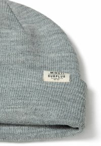 Siva pletena kapa s rebrastom teksturom, s ušivenom etiketom na kojoj piše "MINOTI SURPLUS OUTDOOR EDITION EST. 1997."