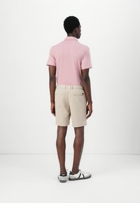 Light pink polo shirt and beige shorts. Polo features a collared neck, and shorts have a relaxed fit with side pockets. Black and white sneakers.