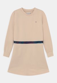 Beżowa sukienka z długim rękawem, prosta podstawa i granatowy pas z napisem "TOMMY HILFIGER" w wielokolorowym tekście. Miękka tkanina.