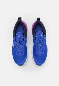 Baskets de sport bleues avec une tige en maille texturée, accents navy, semelle rose et lacets élastiques. Présentent des détails réfléchissants et une languette.