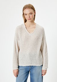 Maglione lavorato a maglia beige chiaro con scollatura a V, maniche lunghe e vestibilità ampia. Il tessuto testurizzato presenta un motivo a costine e una leggera trasparenza.