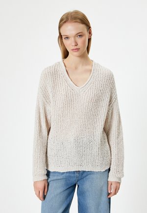 Maglione lavorato a maglia beige chiaro con scollatura a V, maniche lunghe e vestibilità ampia. Il tessuto testurizzato presenta un motivo a costine e una leggera trasparenza.